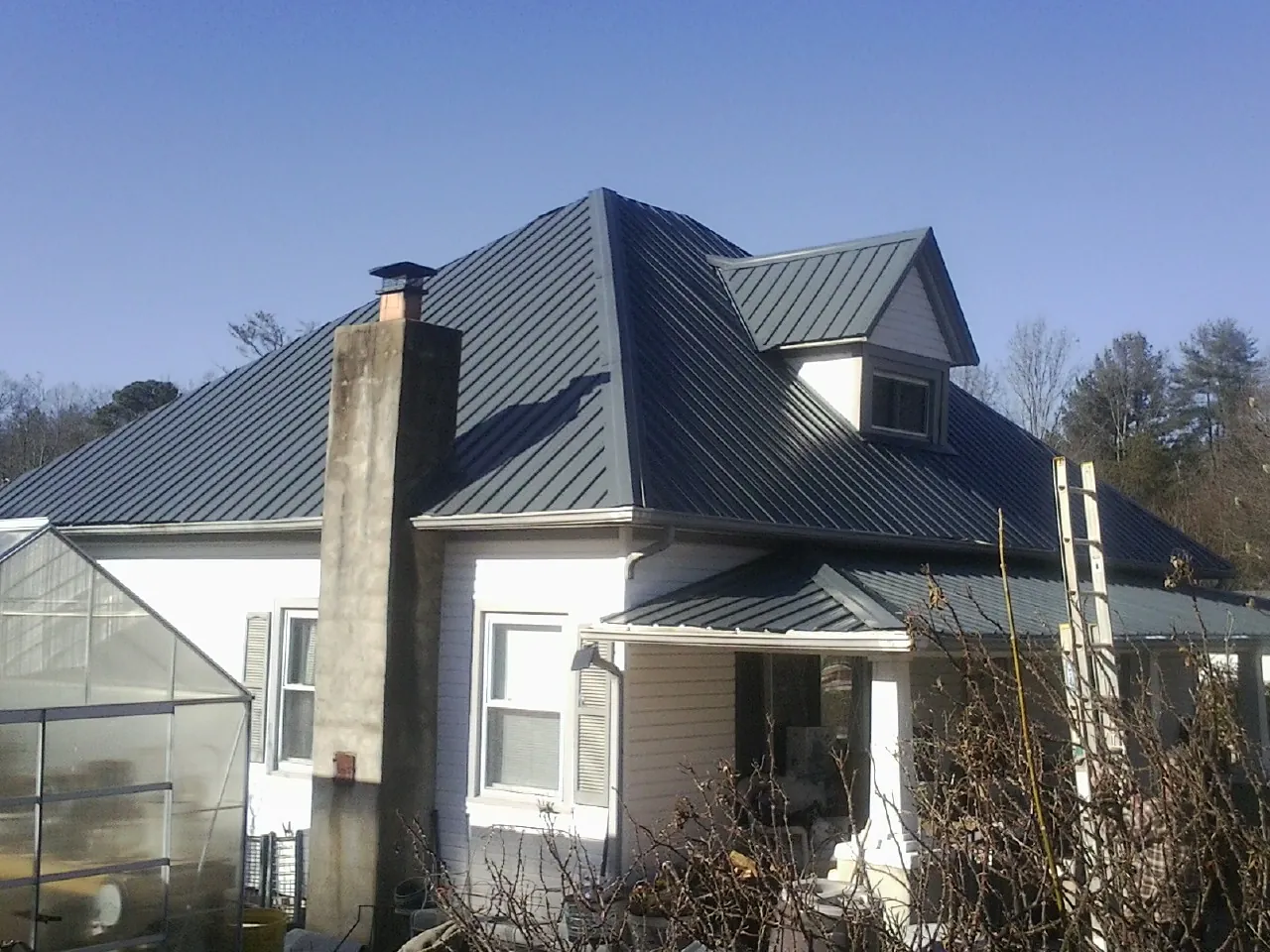 Dark blue standing seam metal roof on a white farmhouse with dormer — Slate & Tile Roof Repair by Roofing Brothers in New Waverly