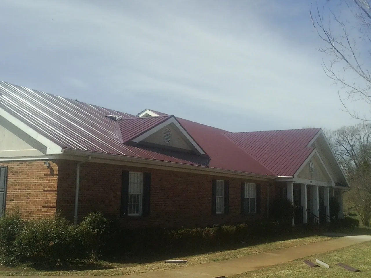 Red metal roof with gabled entries on a long brick building, from a Hail Damage Roof Repair job in New Waverly