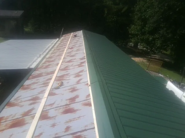 Old rusted panels beside newly installed green metal roofing — Wind Damage Roof Repair by Roofing Brothers in New Waverly