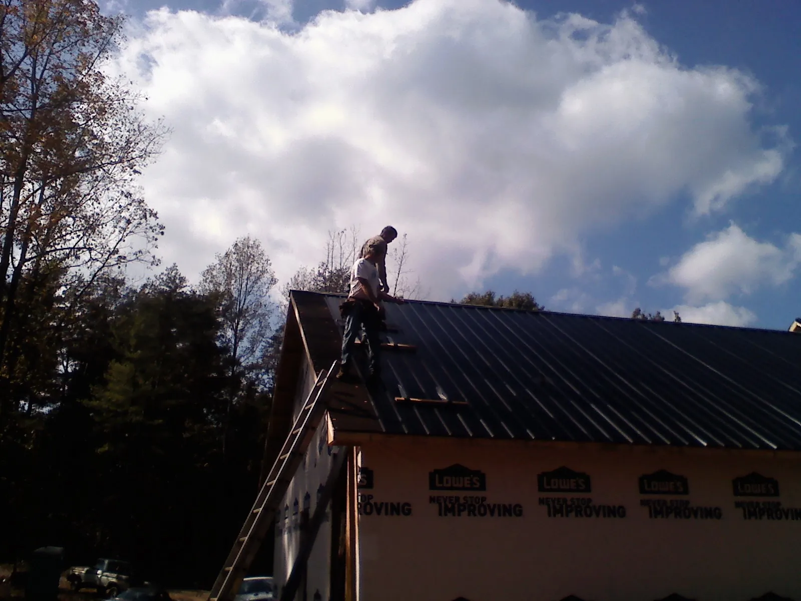 Roofer fastening dark metal panels high against a cloudy sky, from a Roof Inspection job in New Waverly