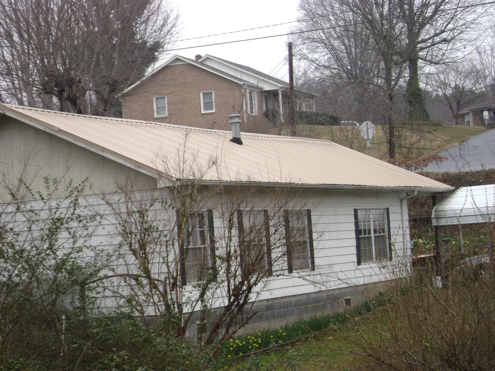 Tan metal roof on a white sided house set into a hillside — Commercial Roofing by Roofing Brothers in New Waverly
