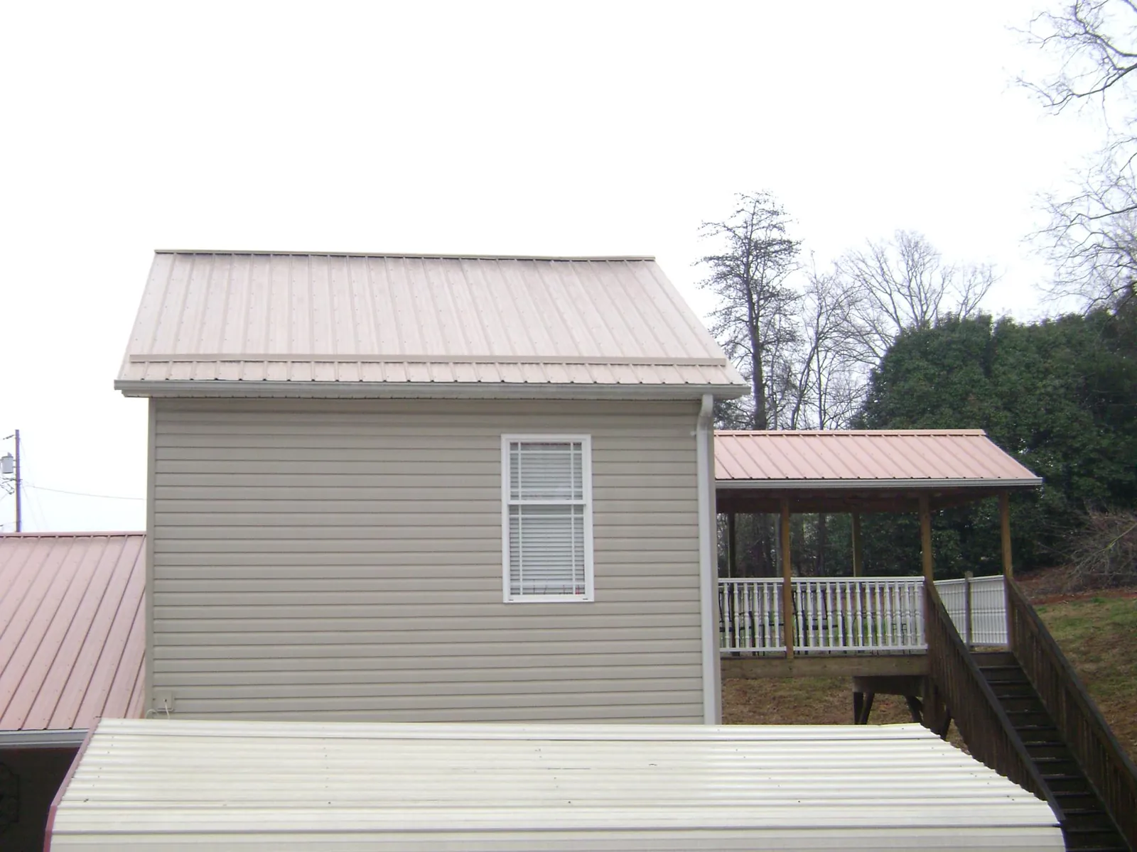 Tan metal roofs on a two story addition and attached porch, from a Roof Replacement job in New Waverly